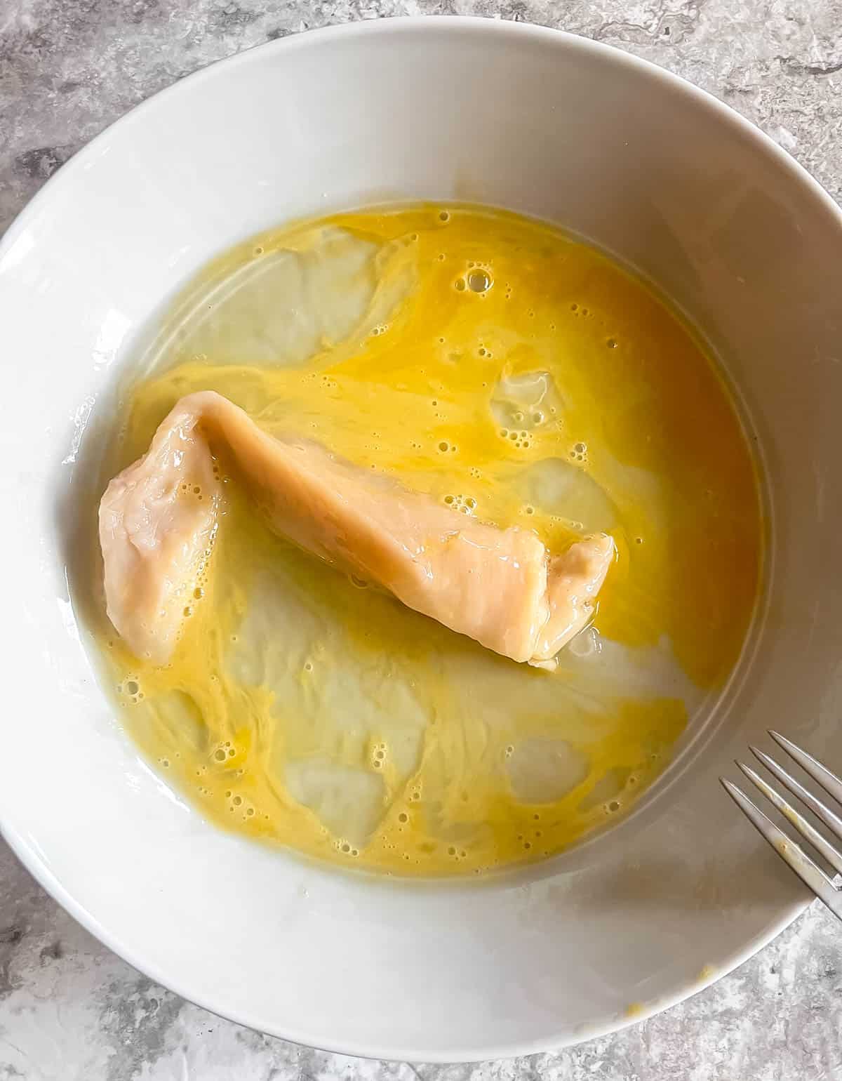 Chicken in egg mixture in bowl.