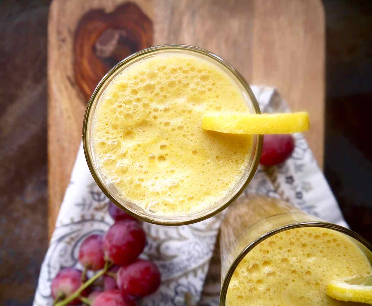 Aerial view of fennel grape juice in two glasses with a lemon on the rim.