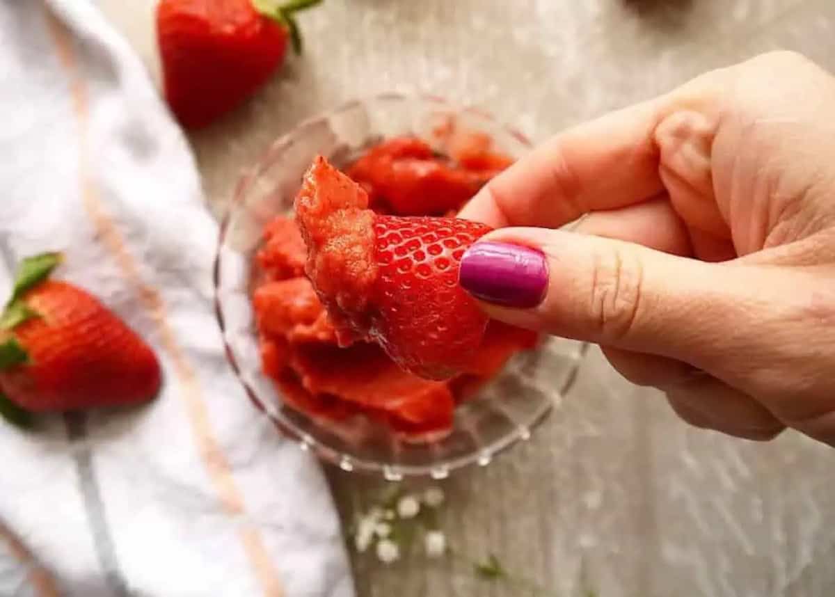 A strawberry dunked into paleo strawberry mango sorbet.