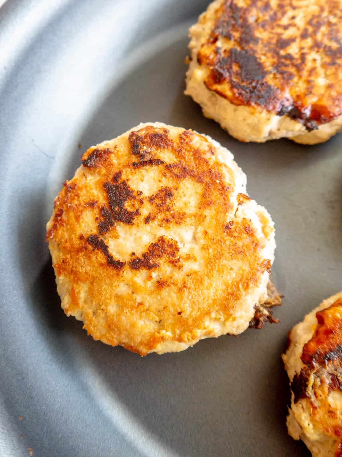 A golden chicken burger patty cooked on a frying pan.