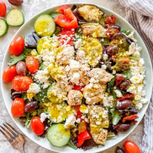 Grilled Chicken Greek Salad in a large plate with dressing on top.