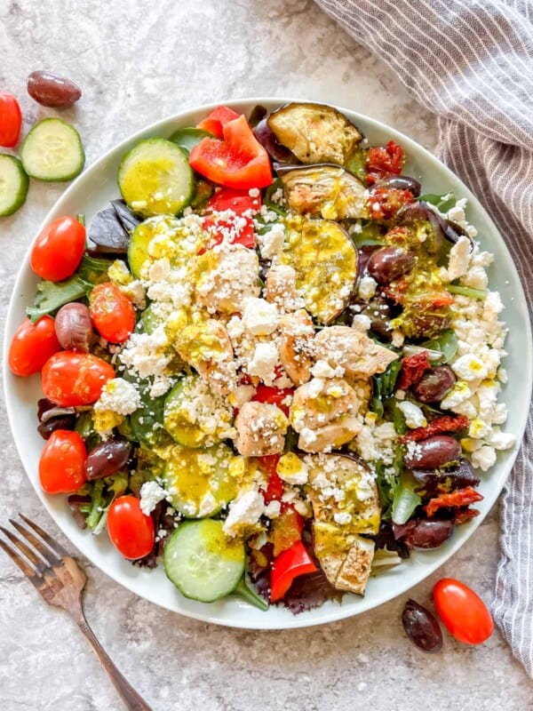 Grilled Chicken Greek Salad in a large plate with dressing on top.