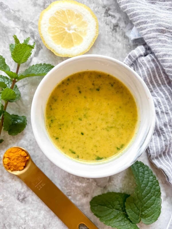 Lemon Turmeric dressing in a bowl surrounded by mint and turmeric.
