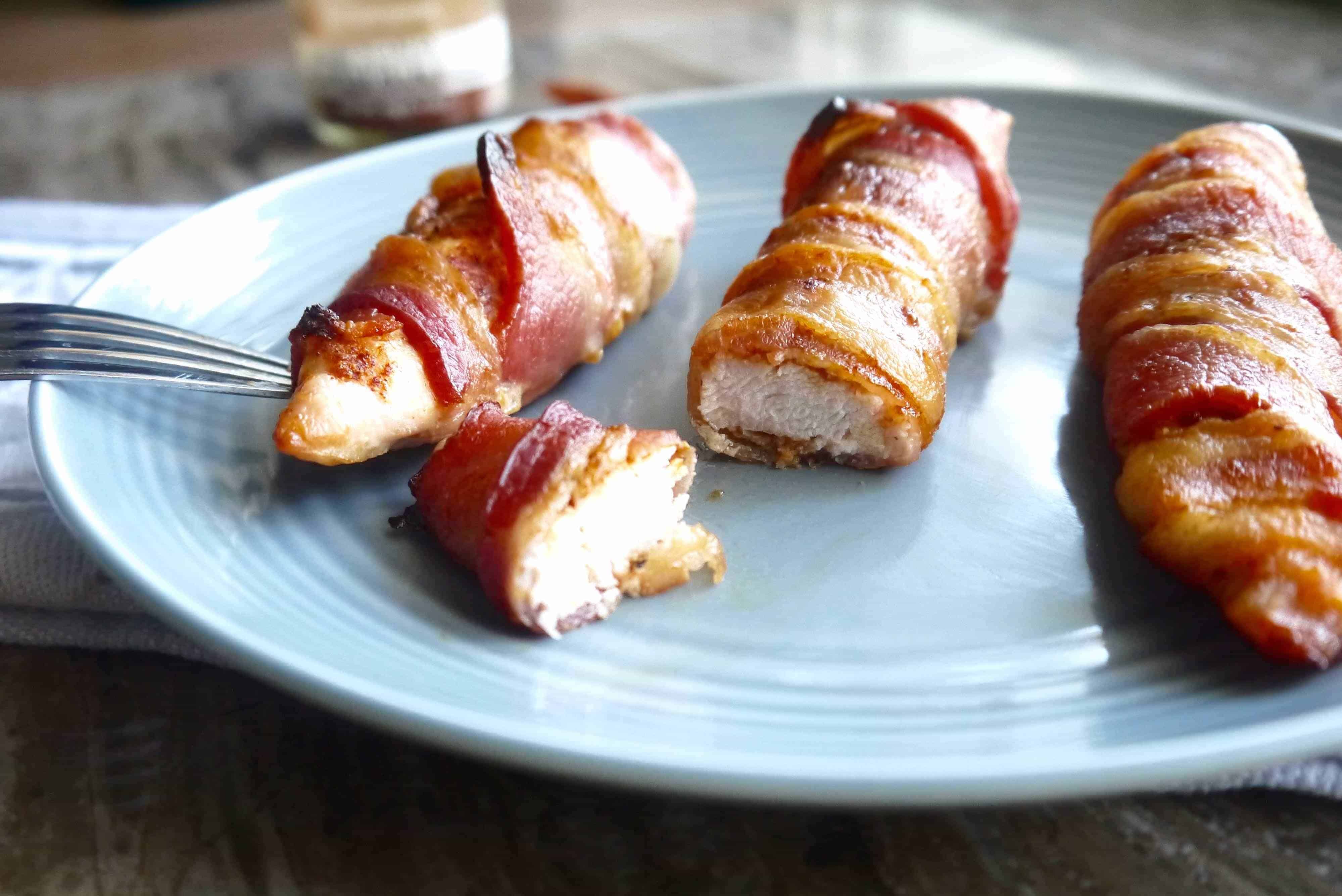 Bacon wrapped chicken tenders on a plate cut into pieces.