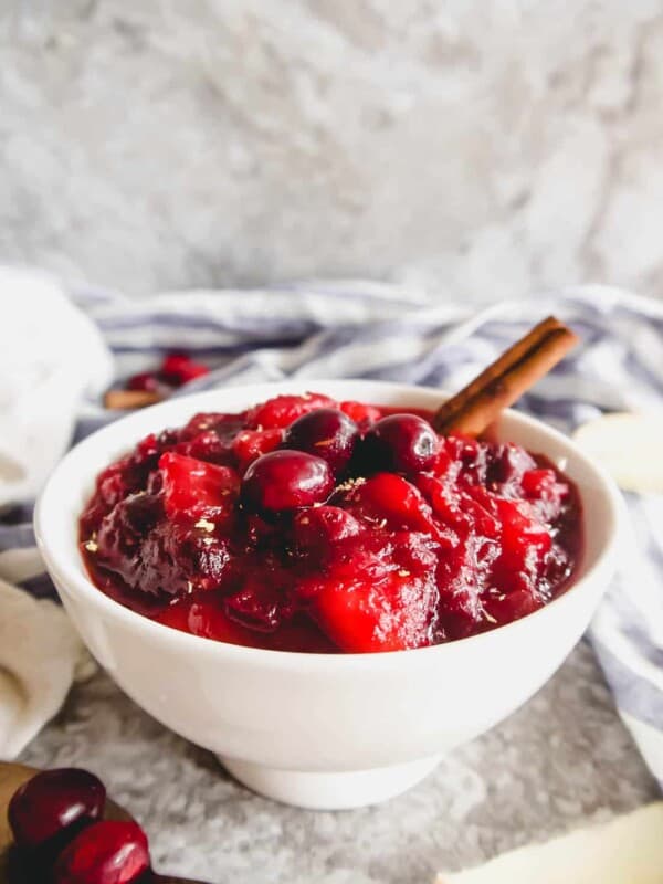Cranberry apple sauce in a bowl with a cinnamon stick in it.