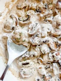 Dairy free mushroom sauce in a pan with a large spoon in it.