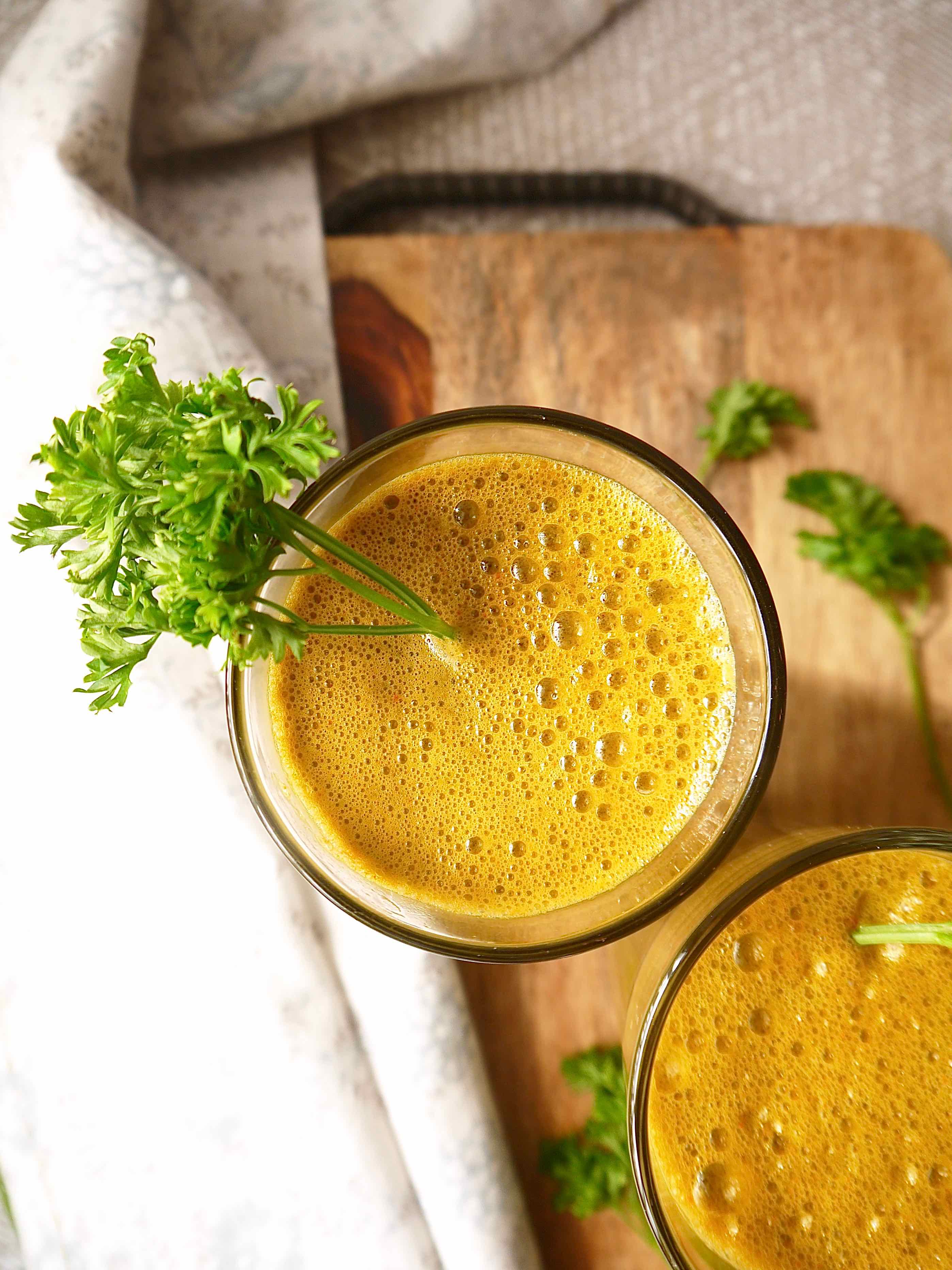 Kale carrot juice in a cup with parsley hanging out.