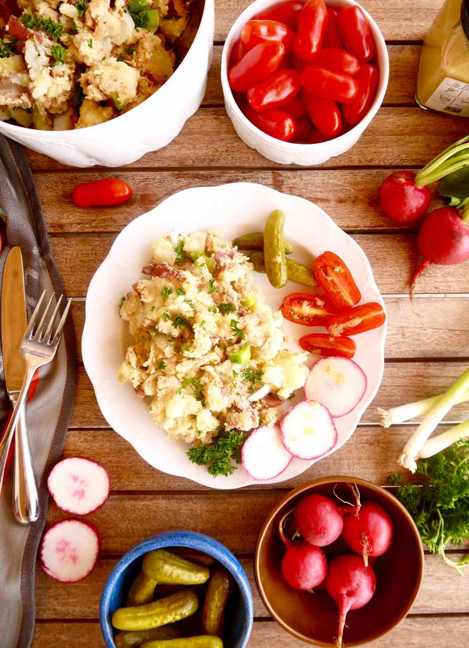 Delicious french potato salad on a plate with tomatoes, radishes, and cornichons.