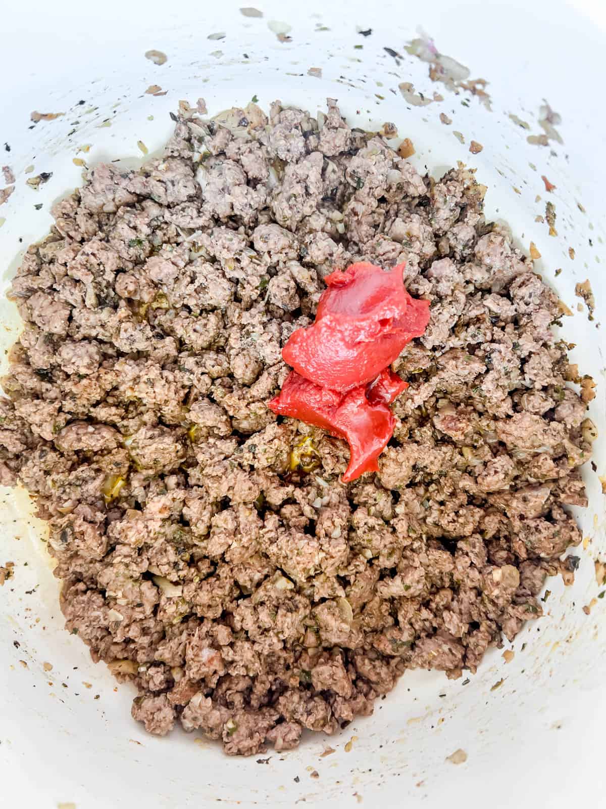 Tomato paste added to ground beef in a pan.