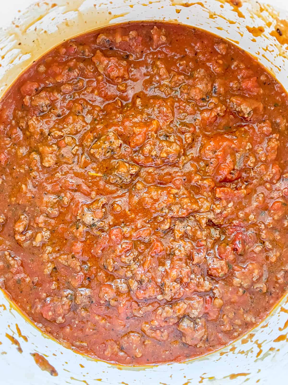 Tomato sauce added to ground beef in a pan.