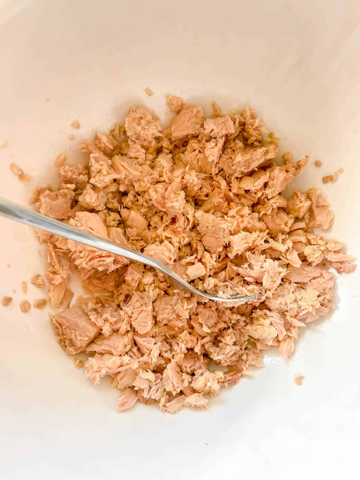 Tuna in a bowl, broken up into pieces by a fork.