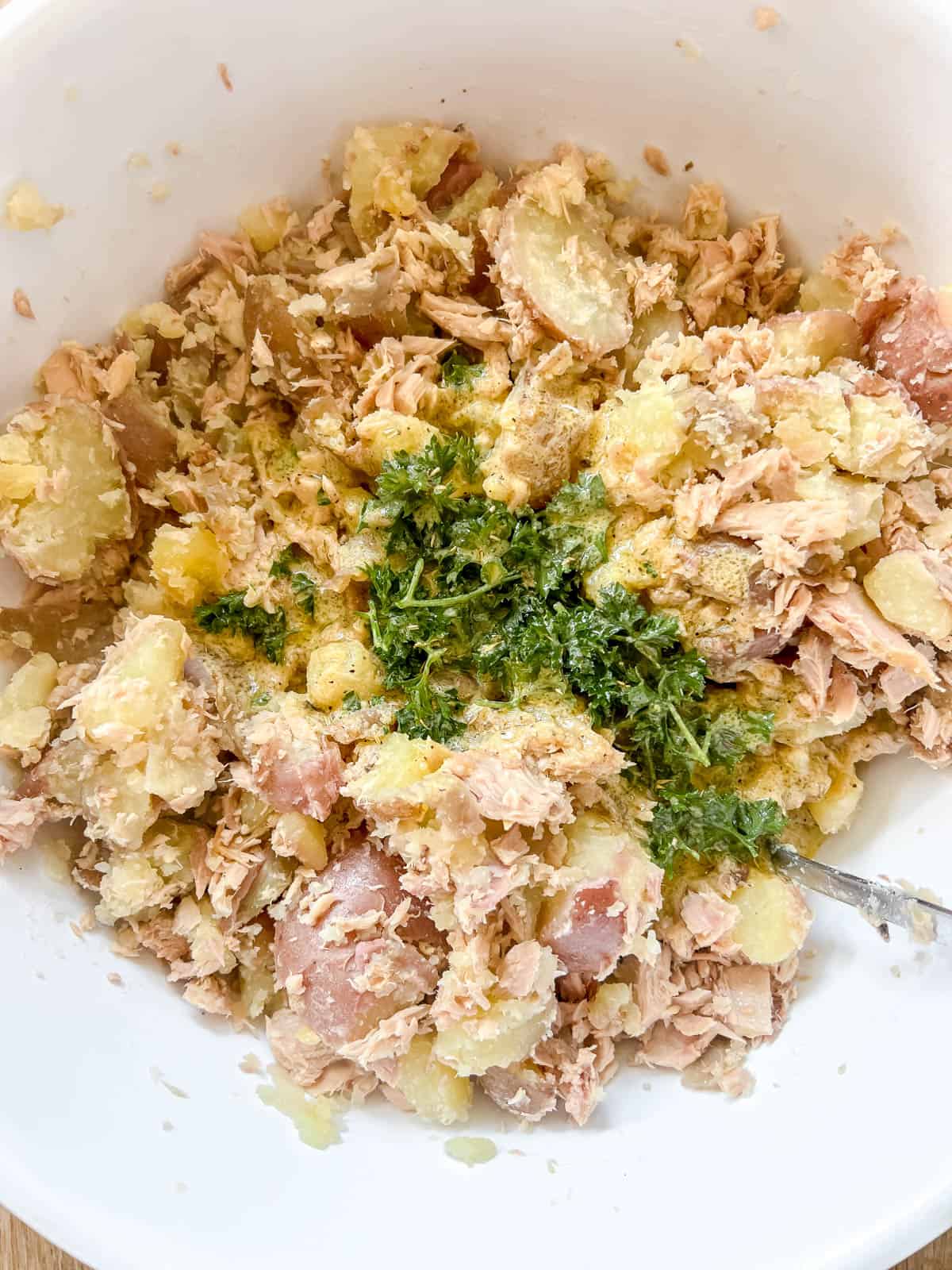Tuna, potatoes and dressing in a bowl.