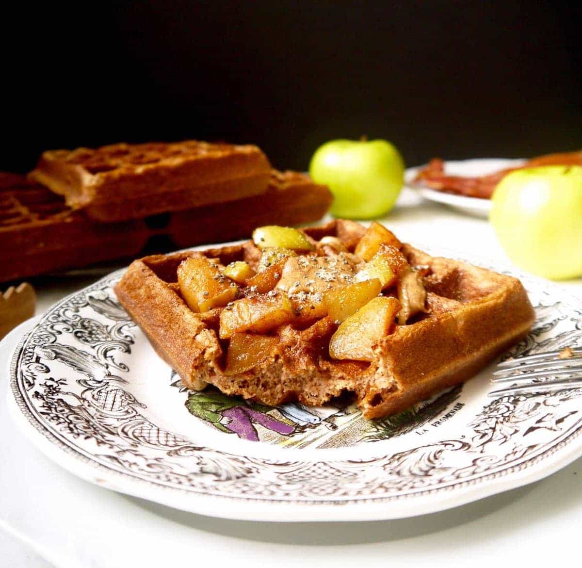 Gluten free apple cinnamon waffles on a plate with a bite taken out of it.