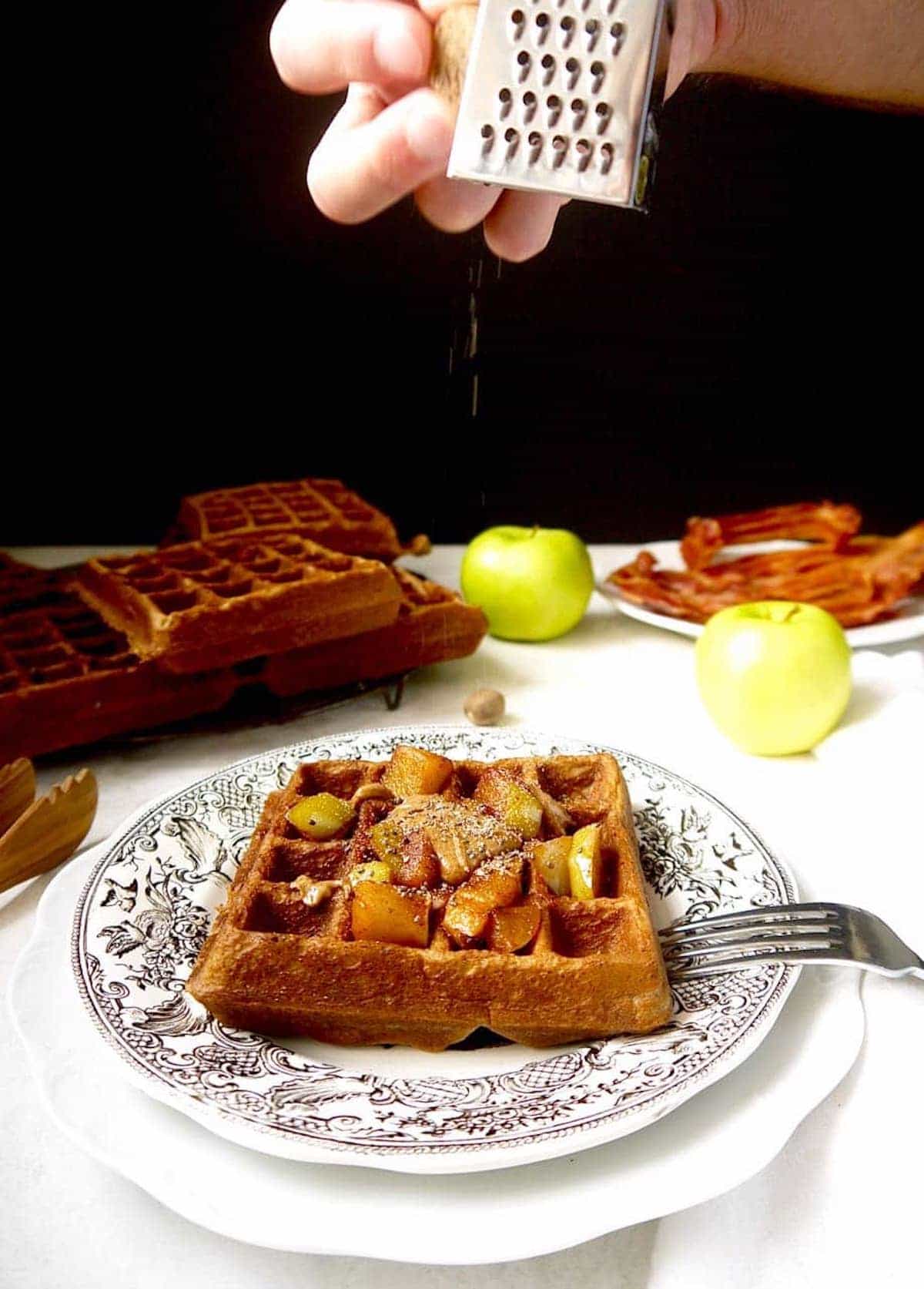 Healthy apple waffles with nutmeg being put on top.