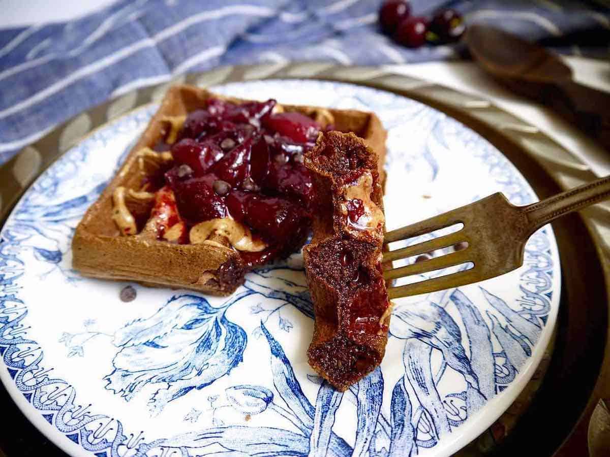 A bite of a chocolate cherry waffle on a fork.
