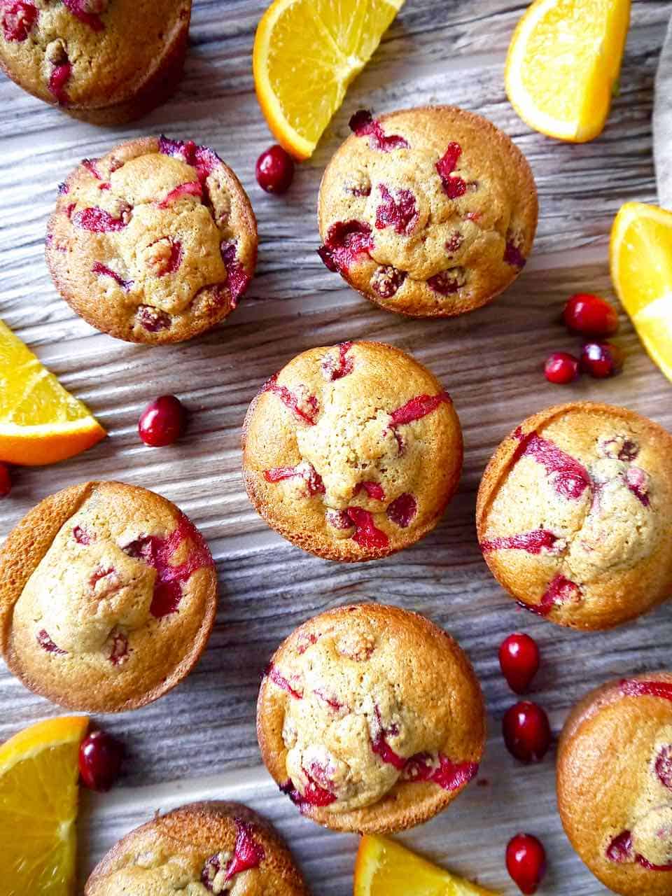 Several orange cranberry muffins on a table surrounded by cranberries.