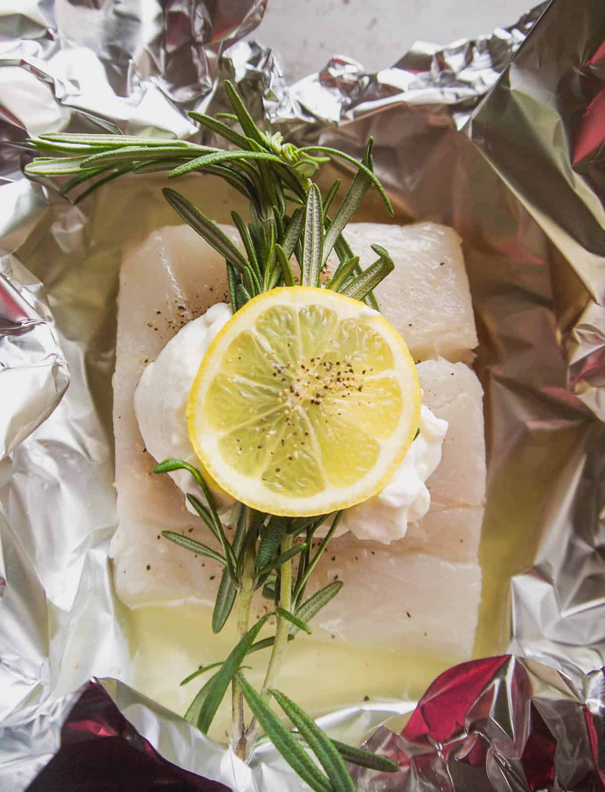Halibut foil packets with lemon and rosemary on top.