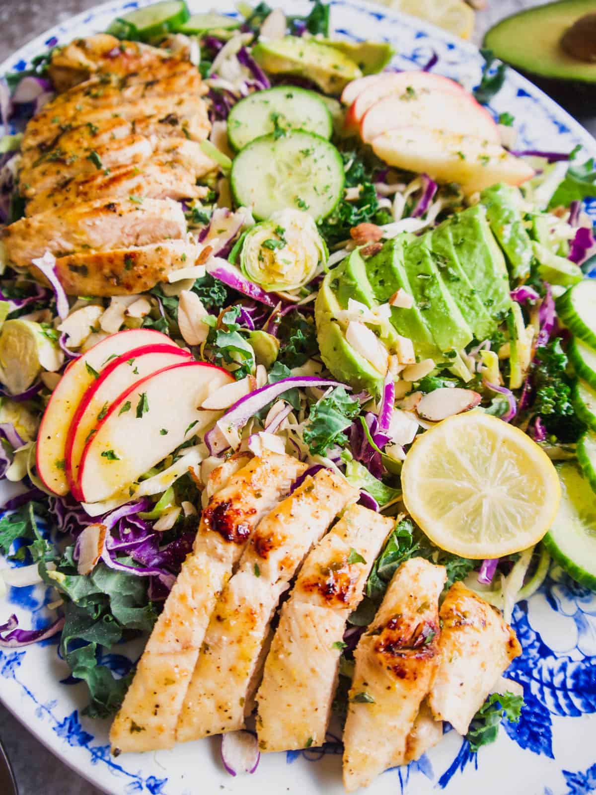 Shredded brussels sprouts salad topped with avocado, apples, almonds and grilled chicken.