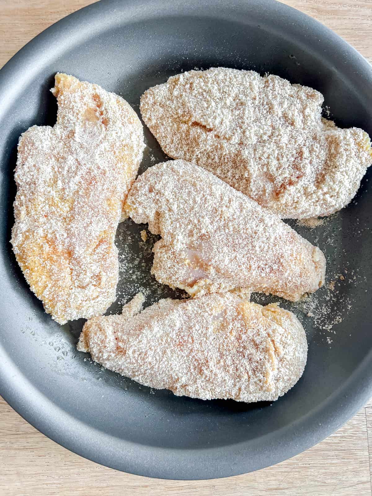 Breaded chicken breast in a pan.