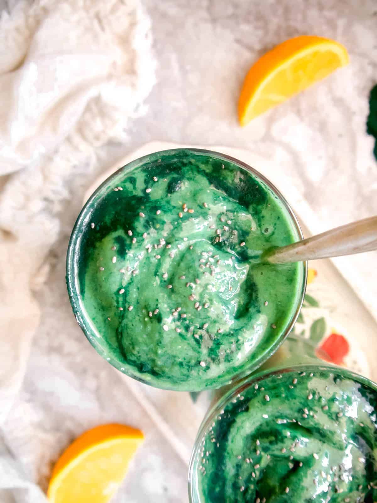Aerial view of mango spirulina smoothie in a cup with a spoon in it.