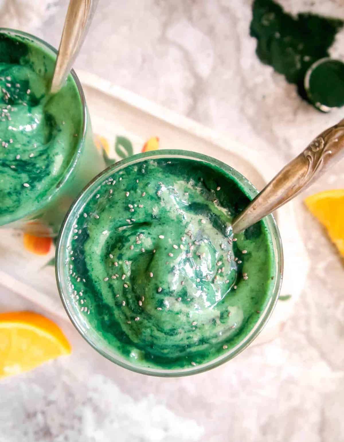 Spirulina Smoothie with Banana, Orange, and Mango in two cups with chia seeds on top.