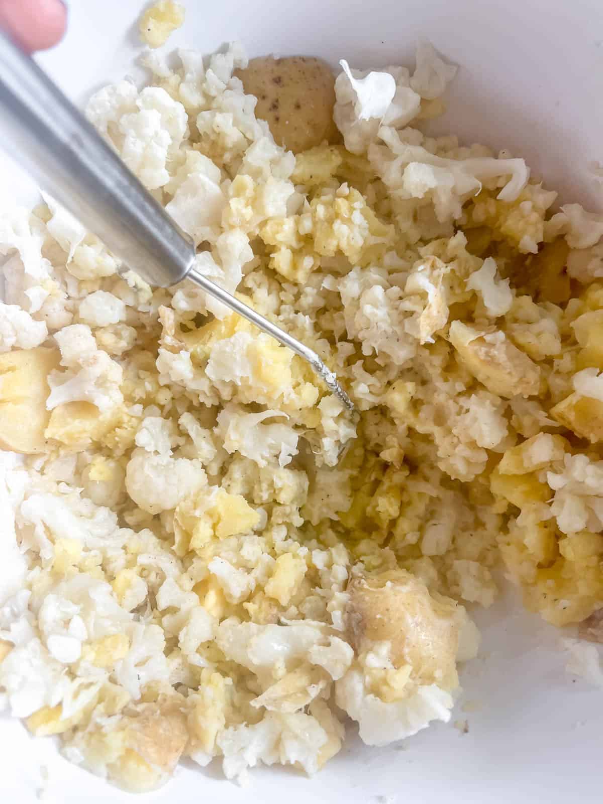 Garlic mashed potatoes and cauliflower being mashed in a bowl.
