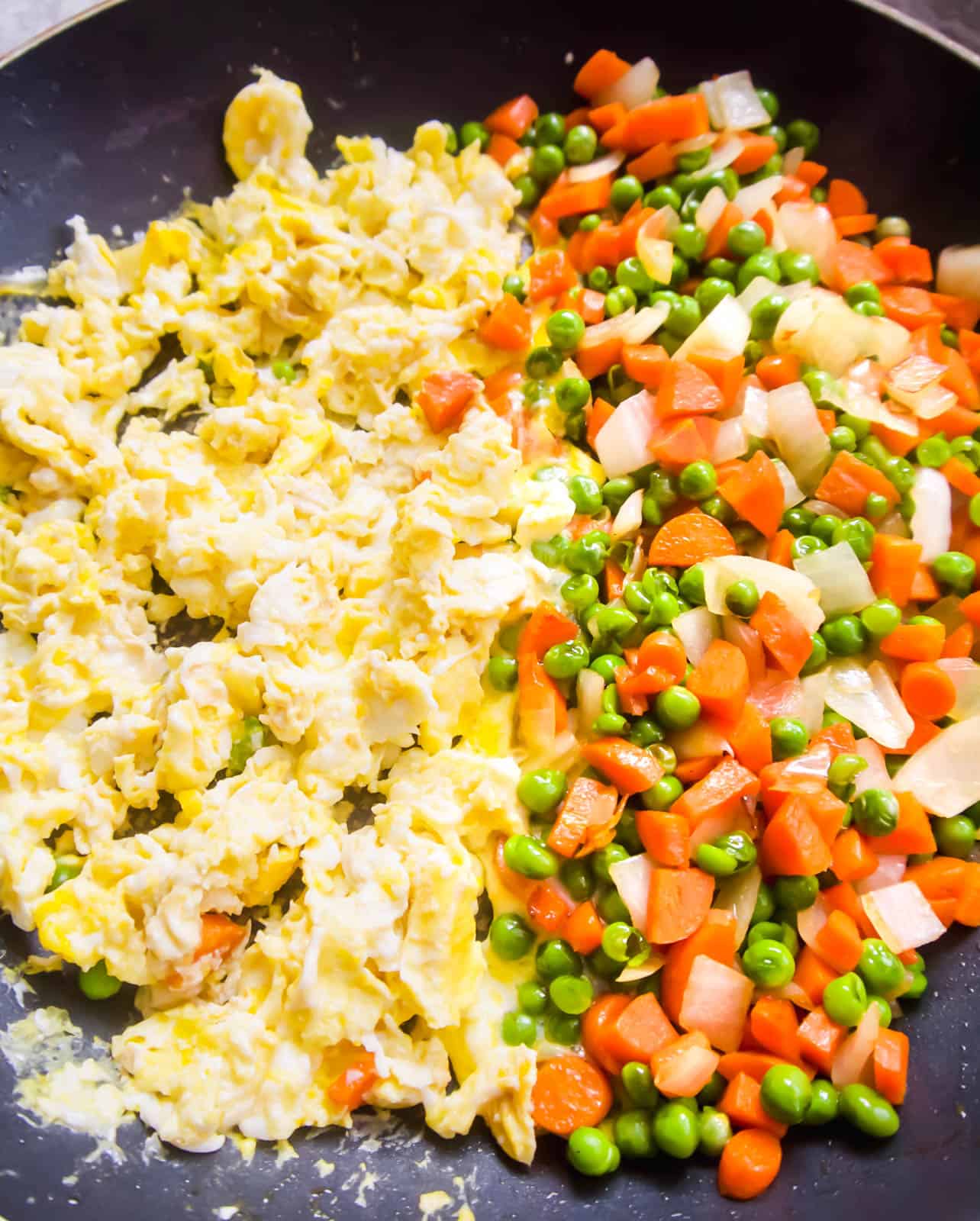 Half the frying pan with scrambled eggs and half with carrots and peas.
