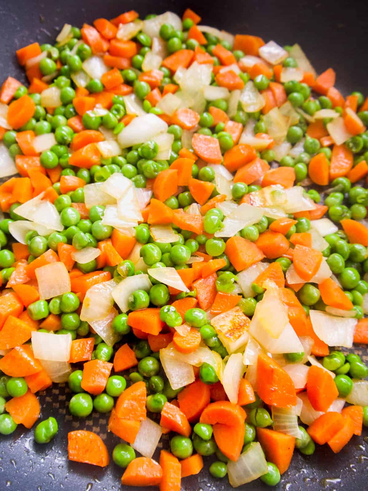 Photo of onion, carrots and peas cooking in frying pan.