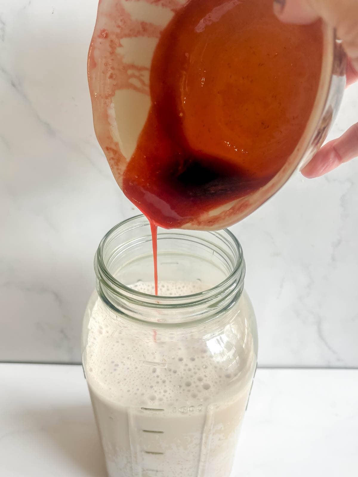 Pouring the strawberry syrup into the almond milk.