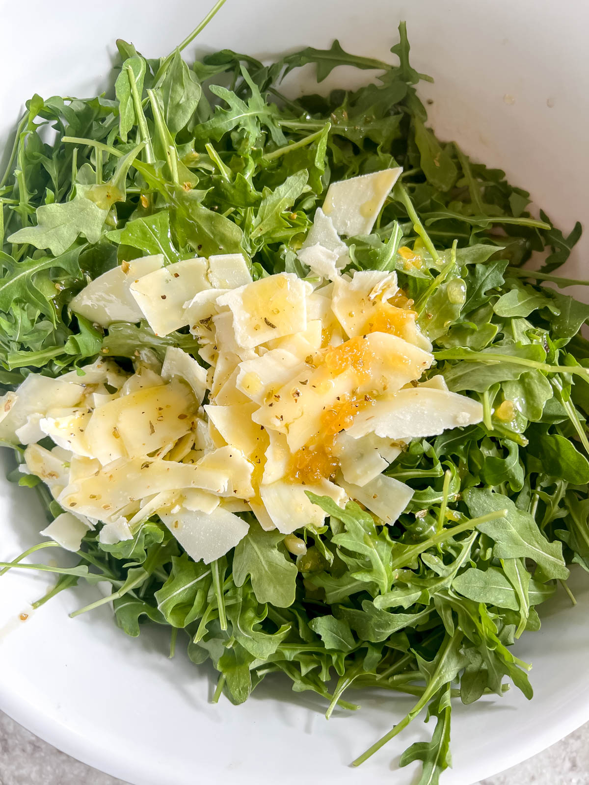 Dressing and parmesan on top of arugula.