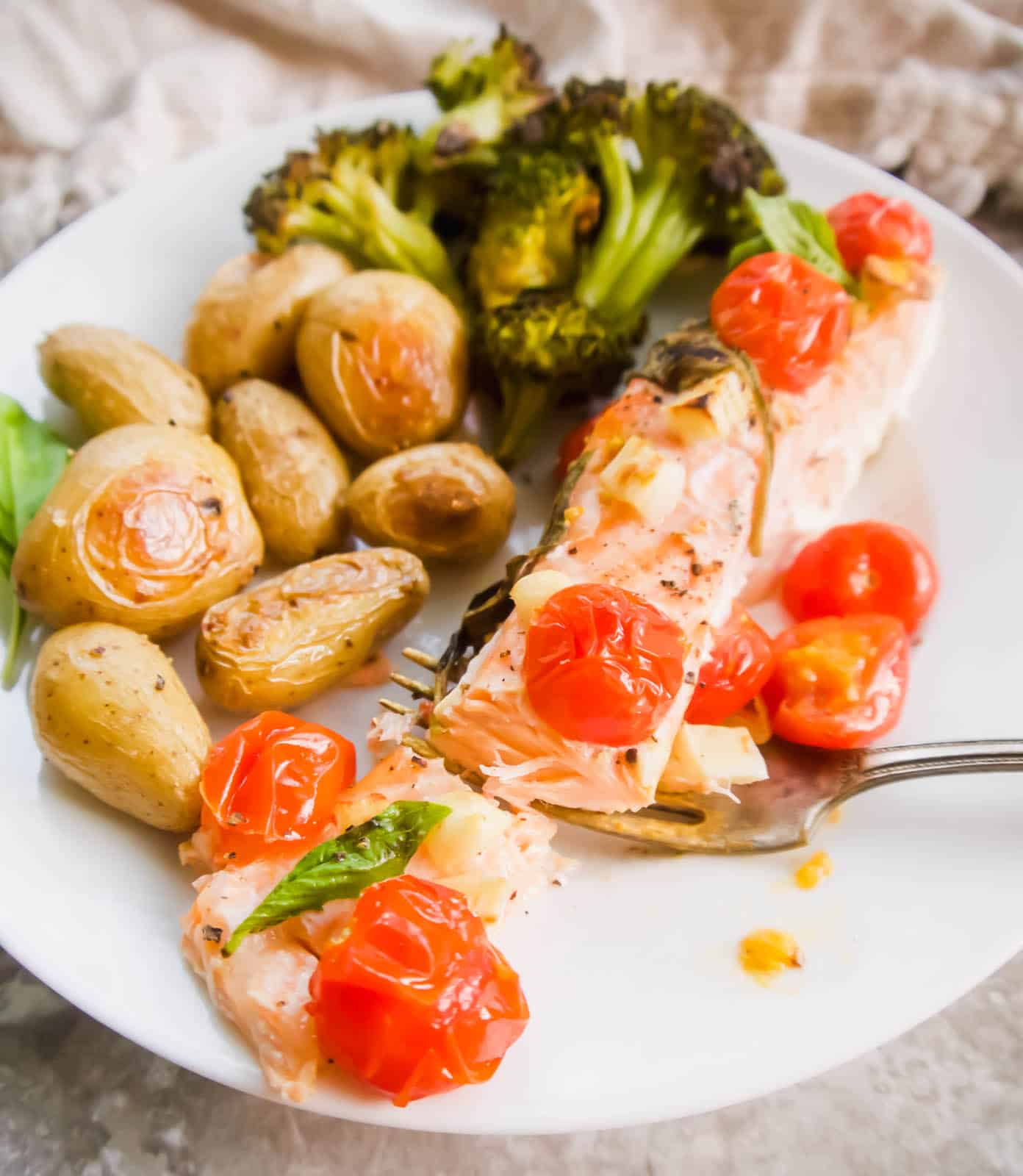Baked salmon with tomatoes on a plate with potatoes and broccoli.