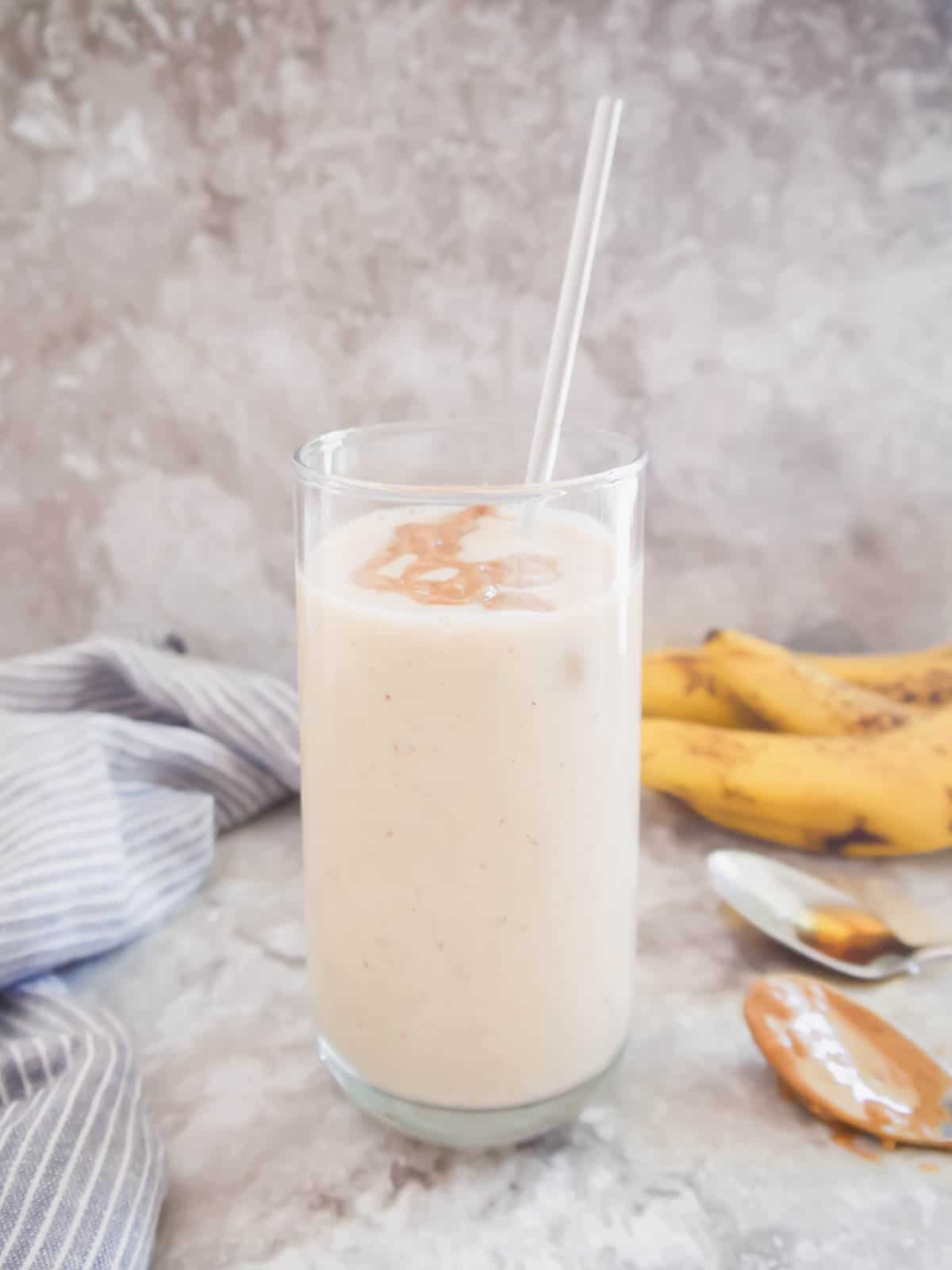 A banana yogurt smoothie with maple syrup in a tall glass with a straw.