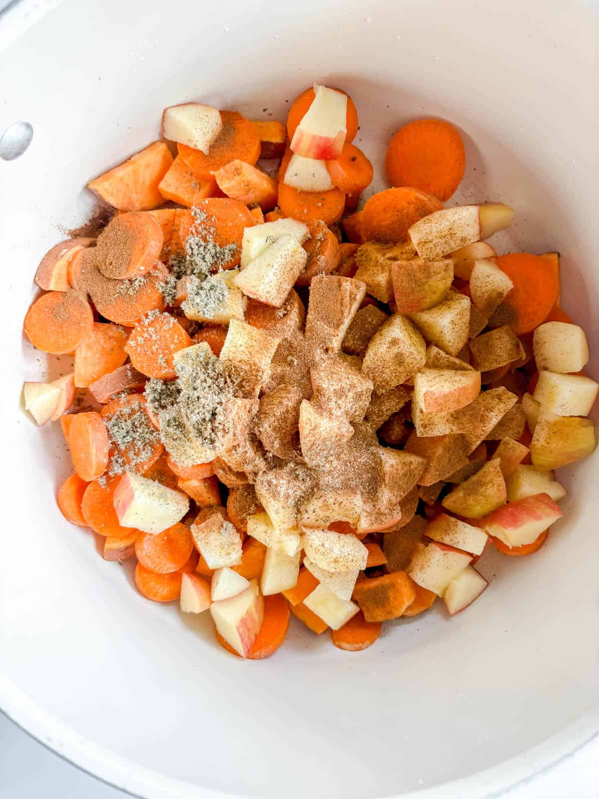 Carrots, sweet potatoes, and apples in a pan with seasoning.