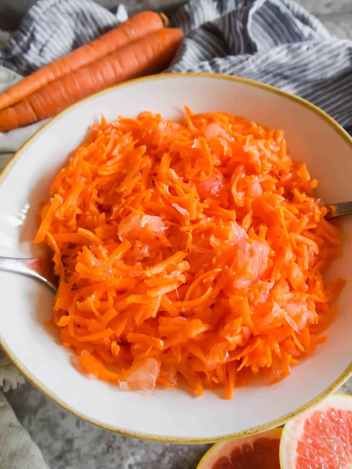 A large bowl of carrot grapefruit salad with spoons inside.