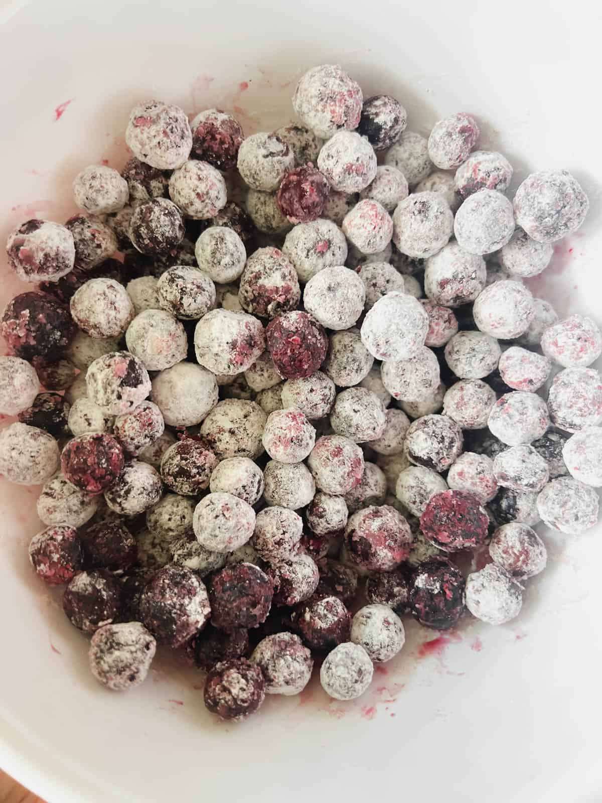 Flour added to frozen blueberries in a bowl.