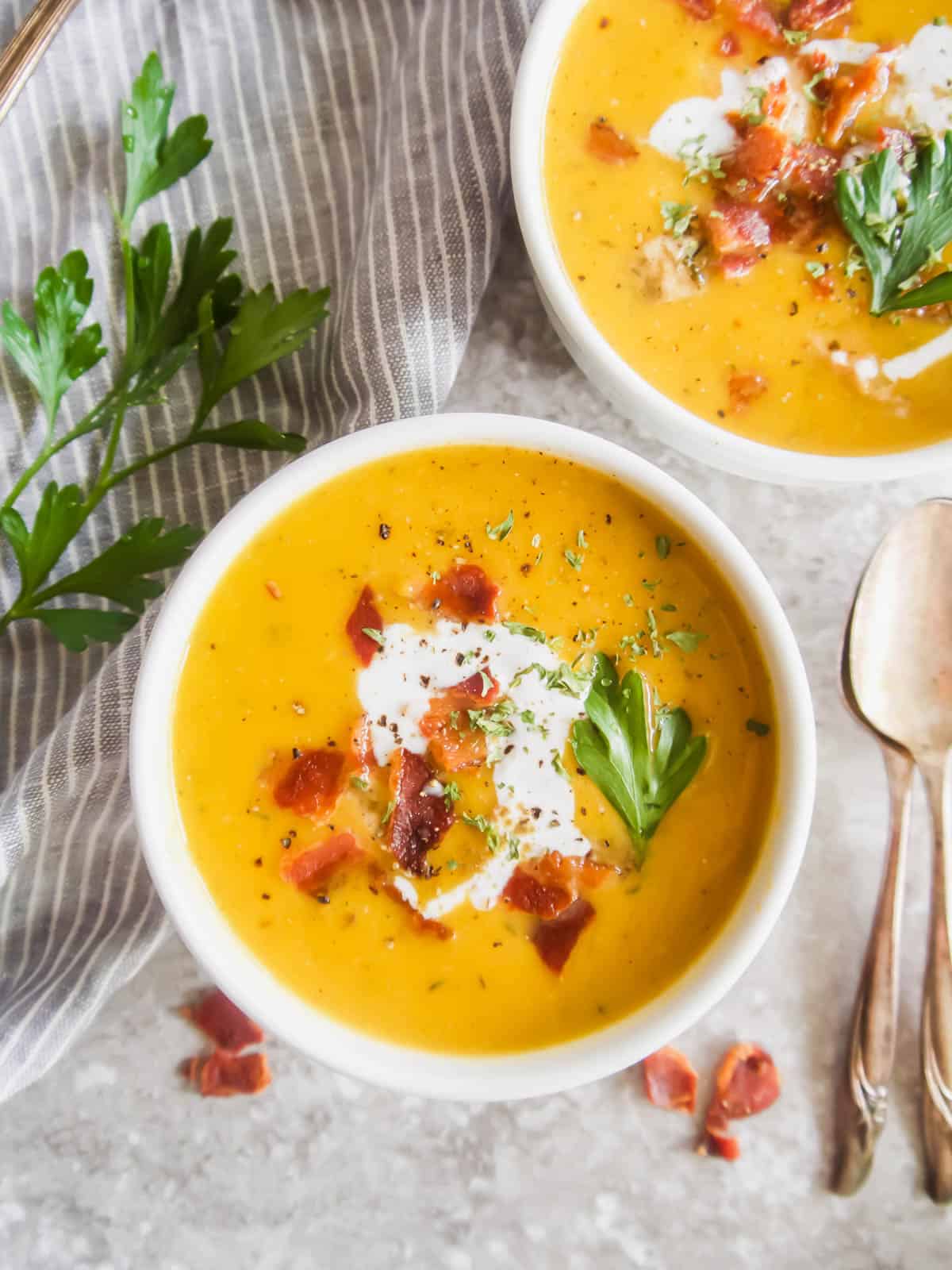 Butternut Squash and Chicken Soup in two bowls with bacon and coconut cream on top.