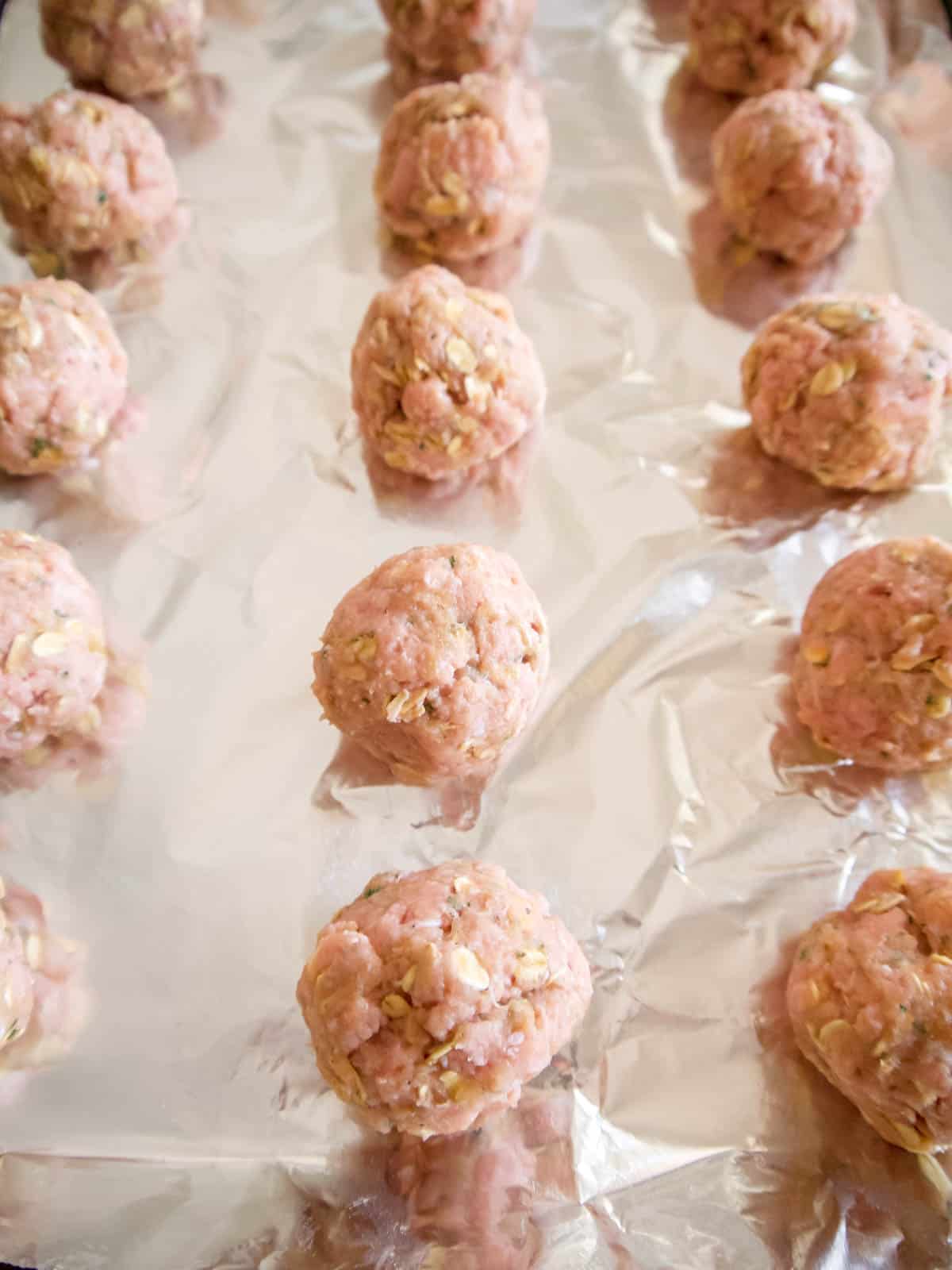 Raw meatballs rolled into a ball on a cookie sheet.