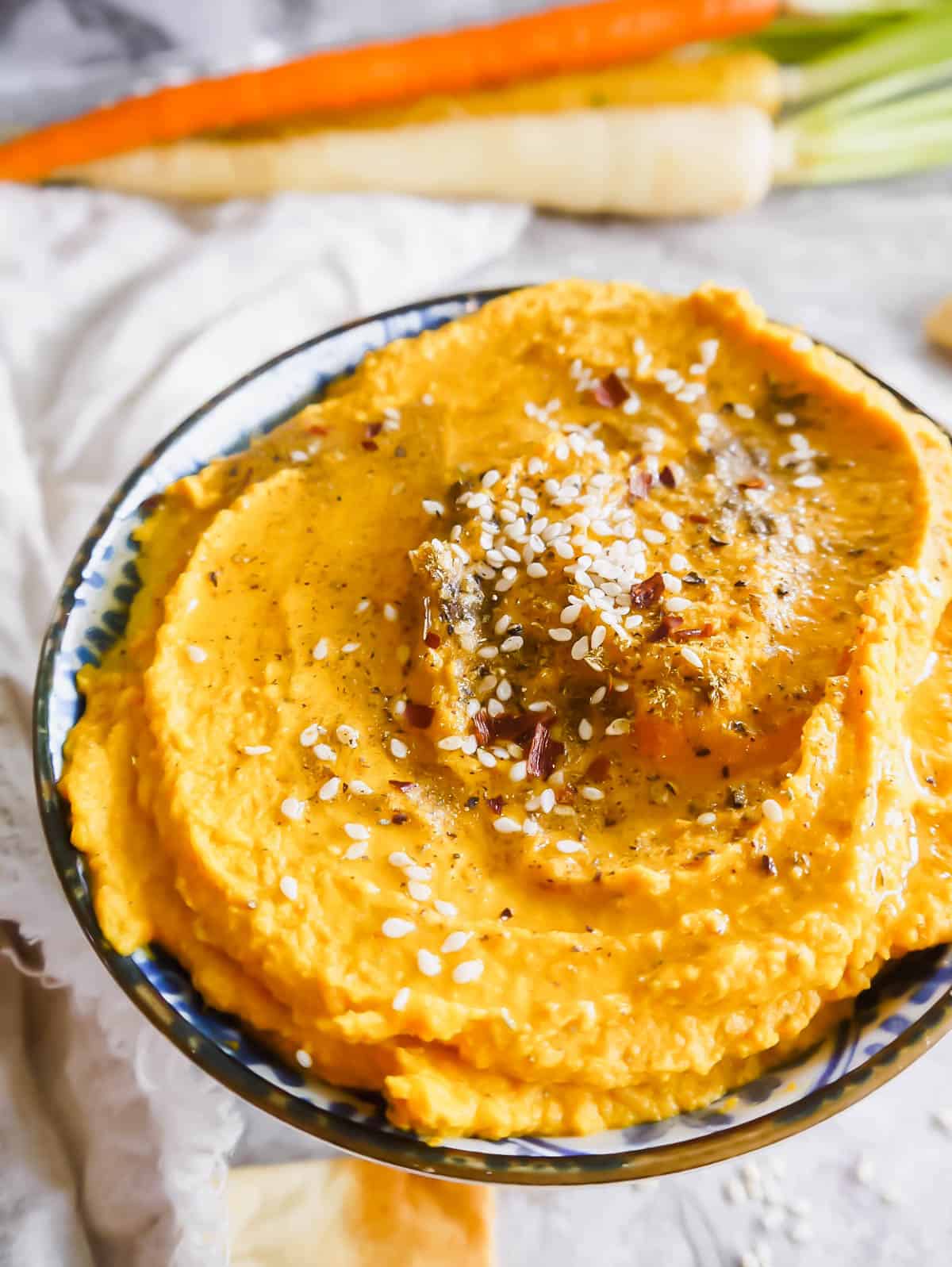 Up close side angle of roasted carrot hummus with sesame seeds, chili flakes and za'atar on top.