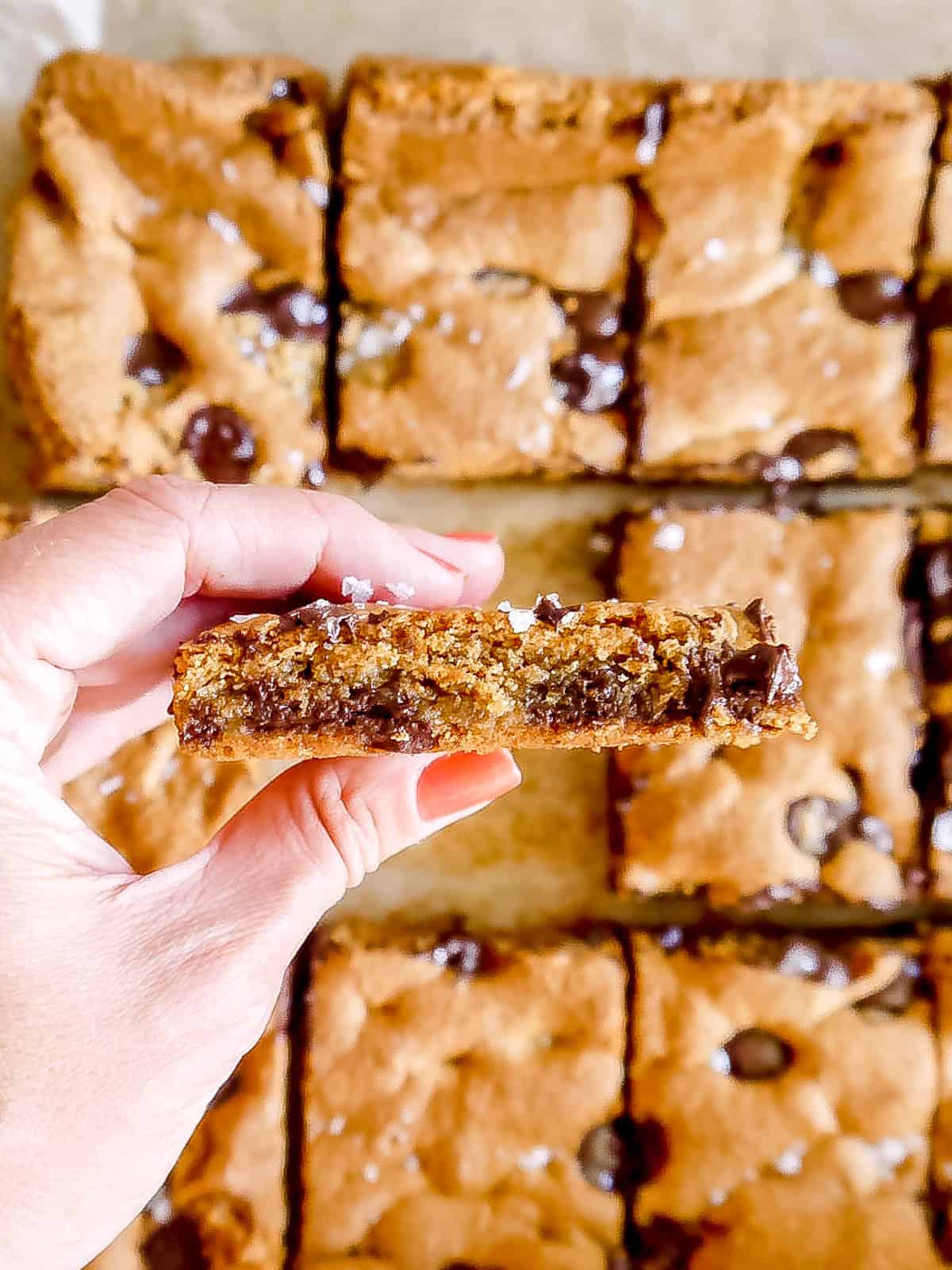 Gluten-free chocolate chip cookie bars in hand about to be bitten.
