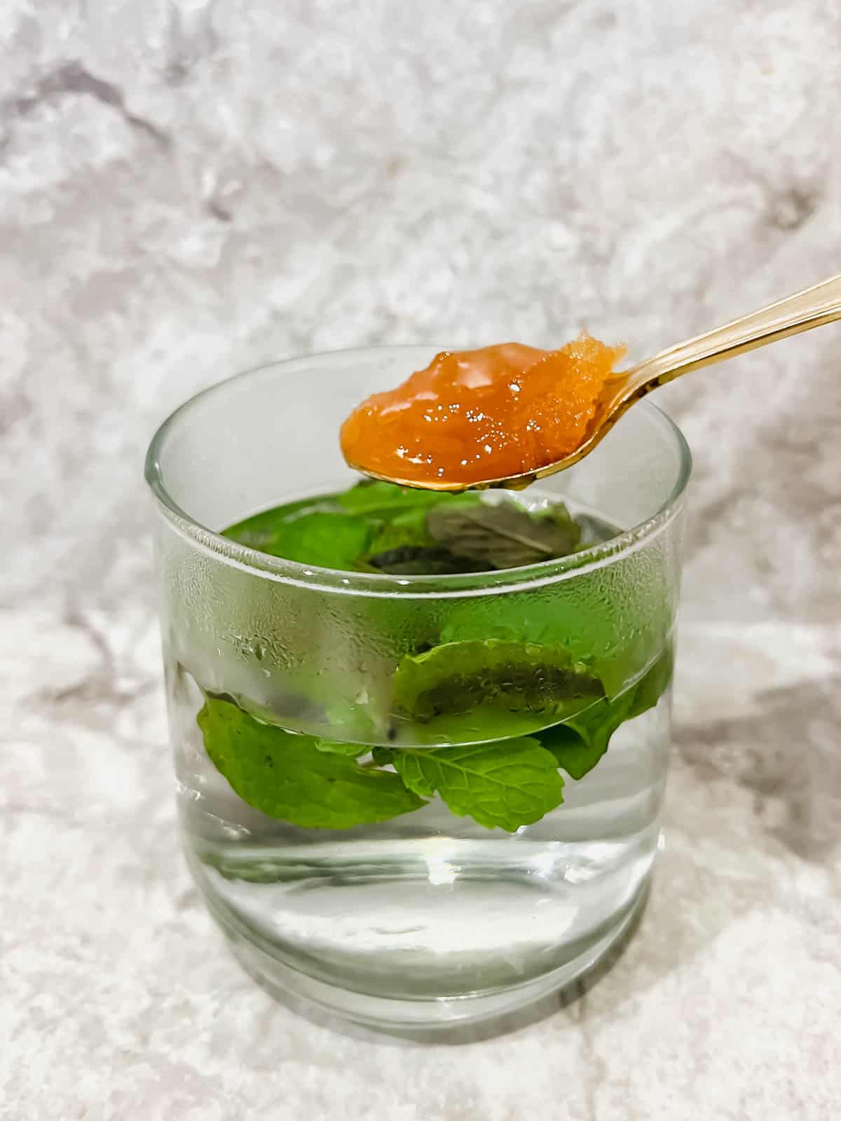 Hot water with mint leaves inside and honey about to be mixed in.