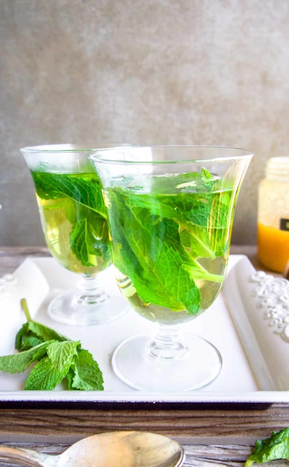 Side angle of mint tea in a cup with mint leaves inside.