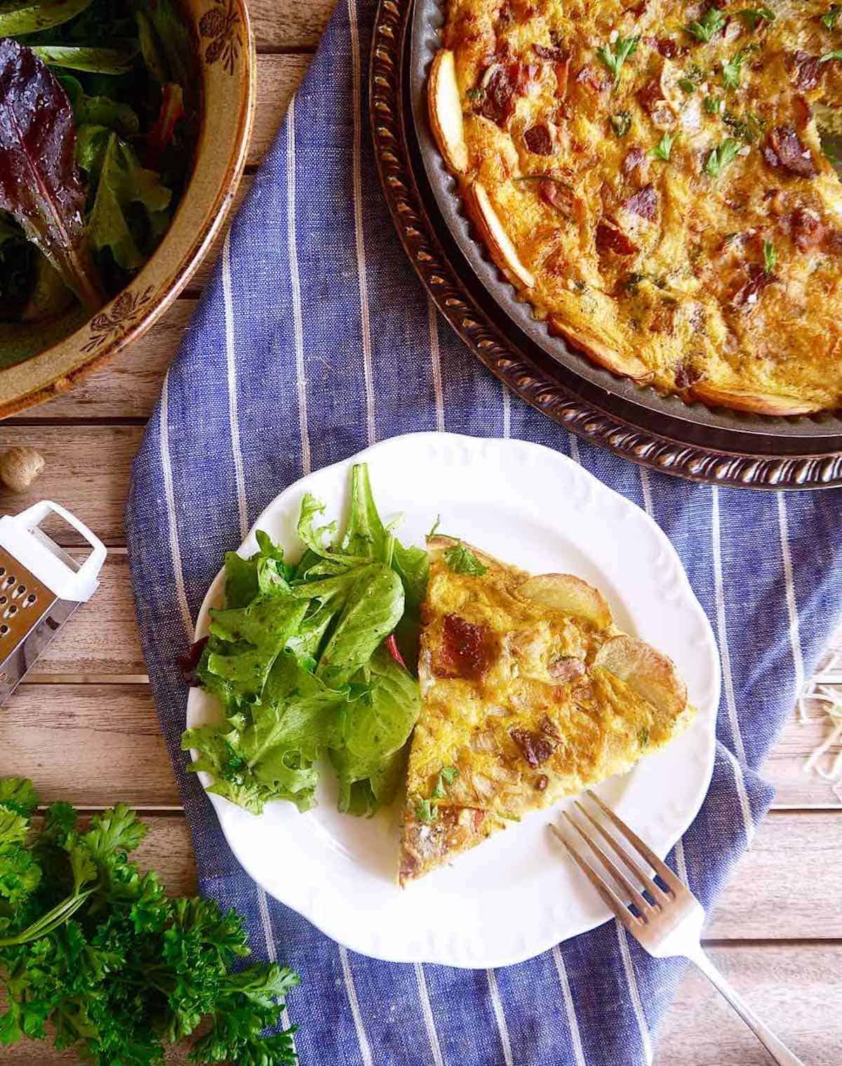 A slice of quiche Lorraine with a side salad on a plate.