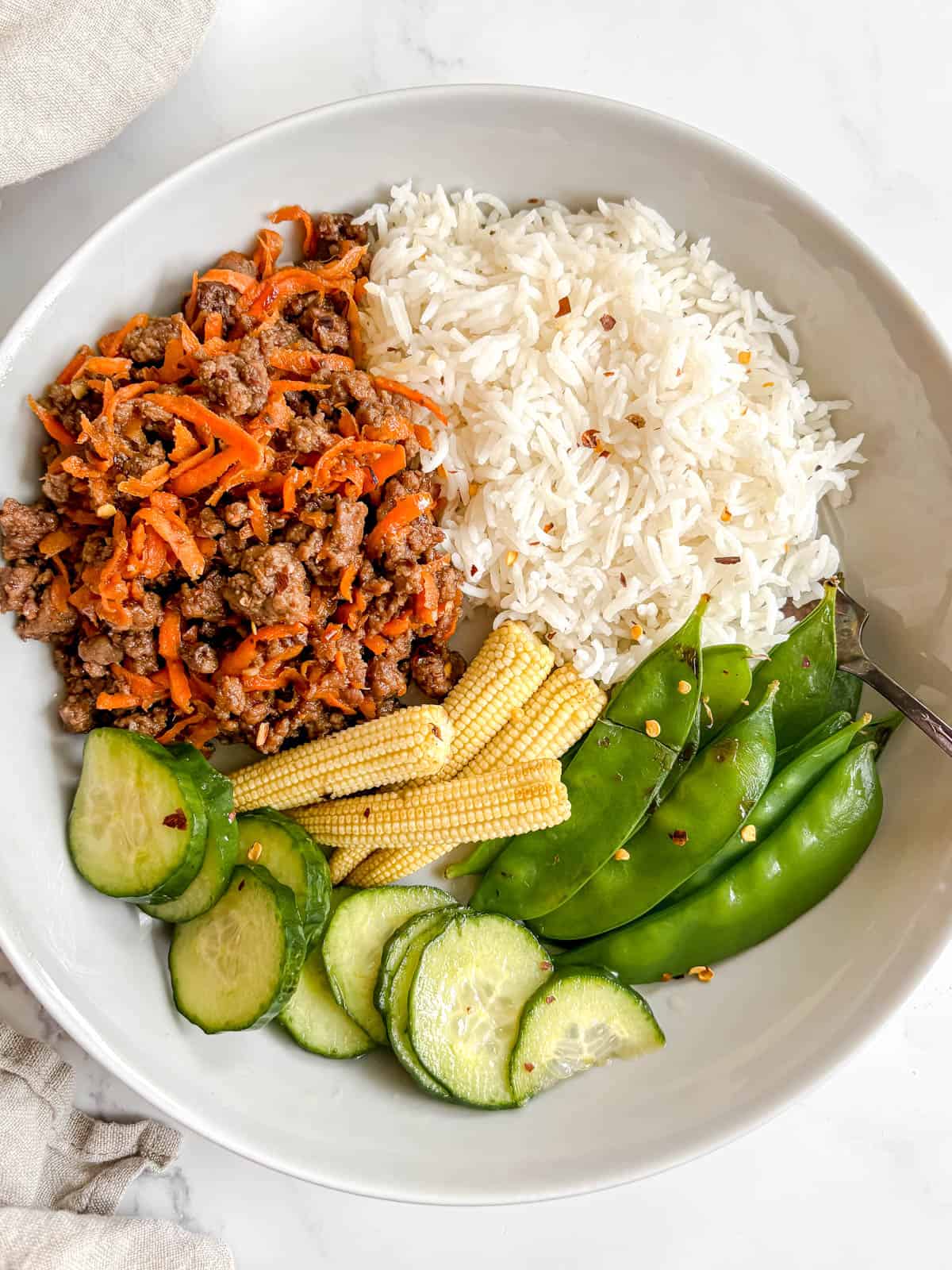 Korean ground beef bowl with rice, snap peas, corn and cucumbers.