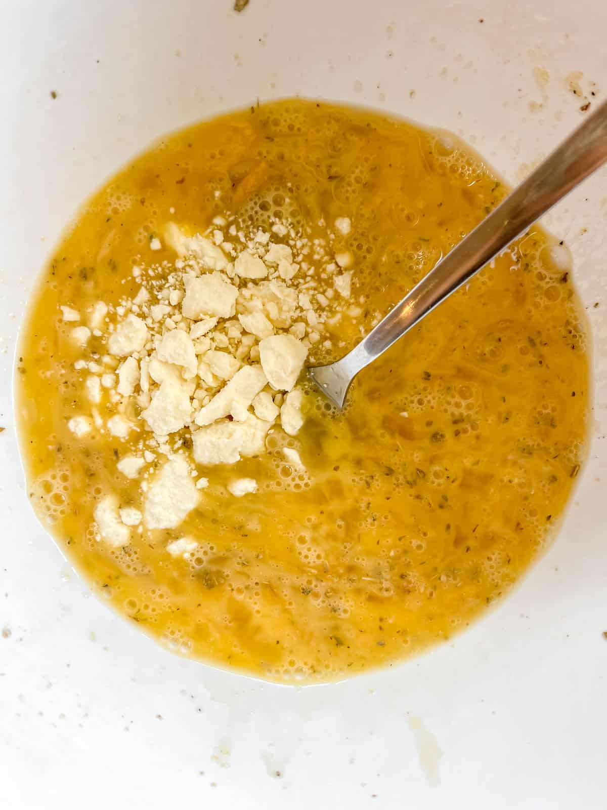 Feta and spices added to eggs in a bowl.