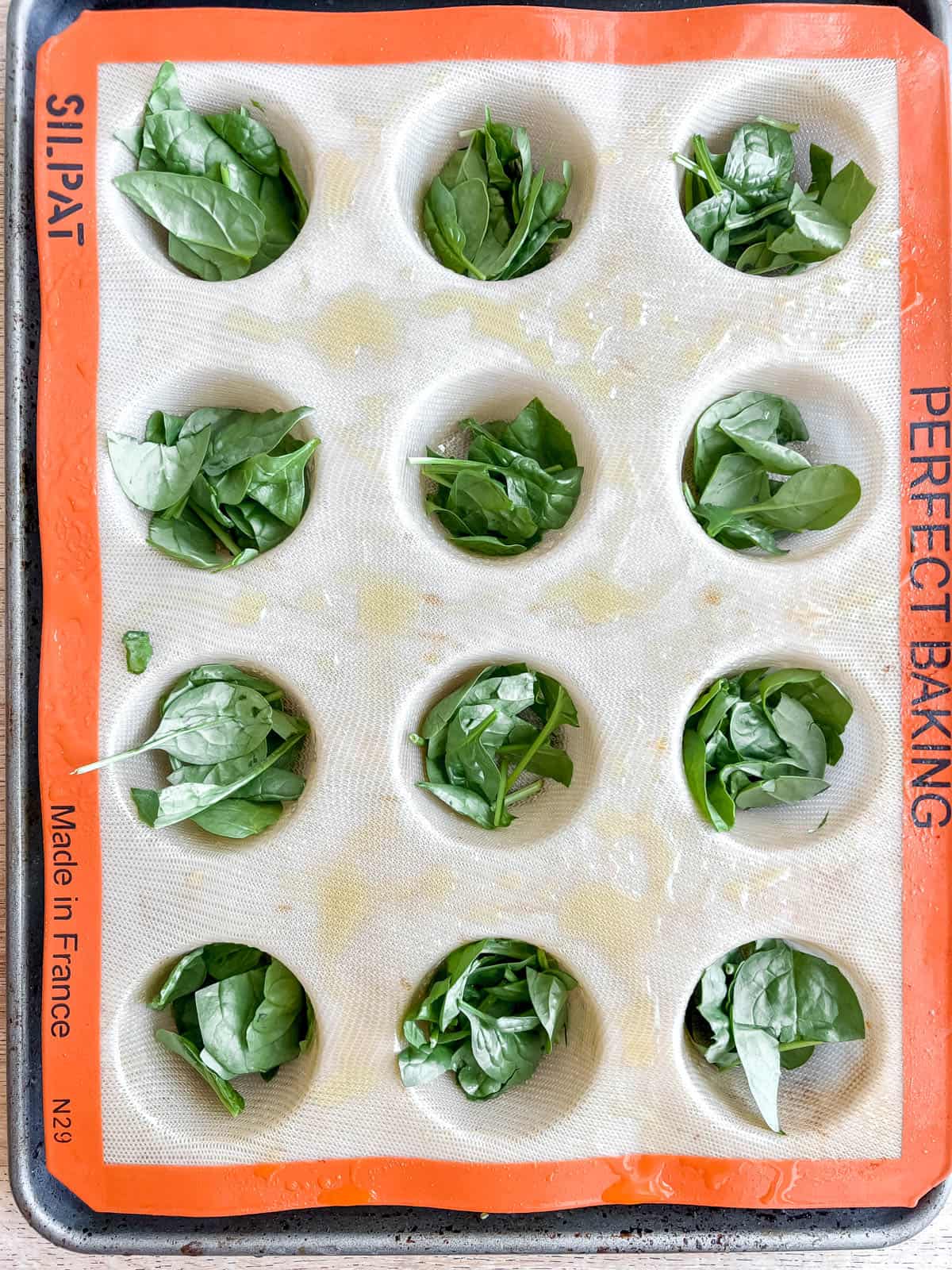 Chopped spinach added to muffin tins.