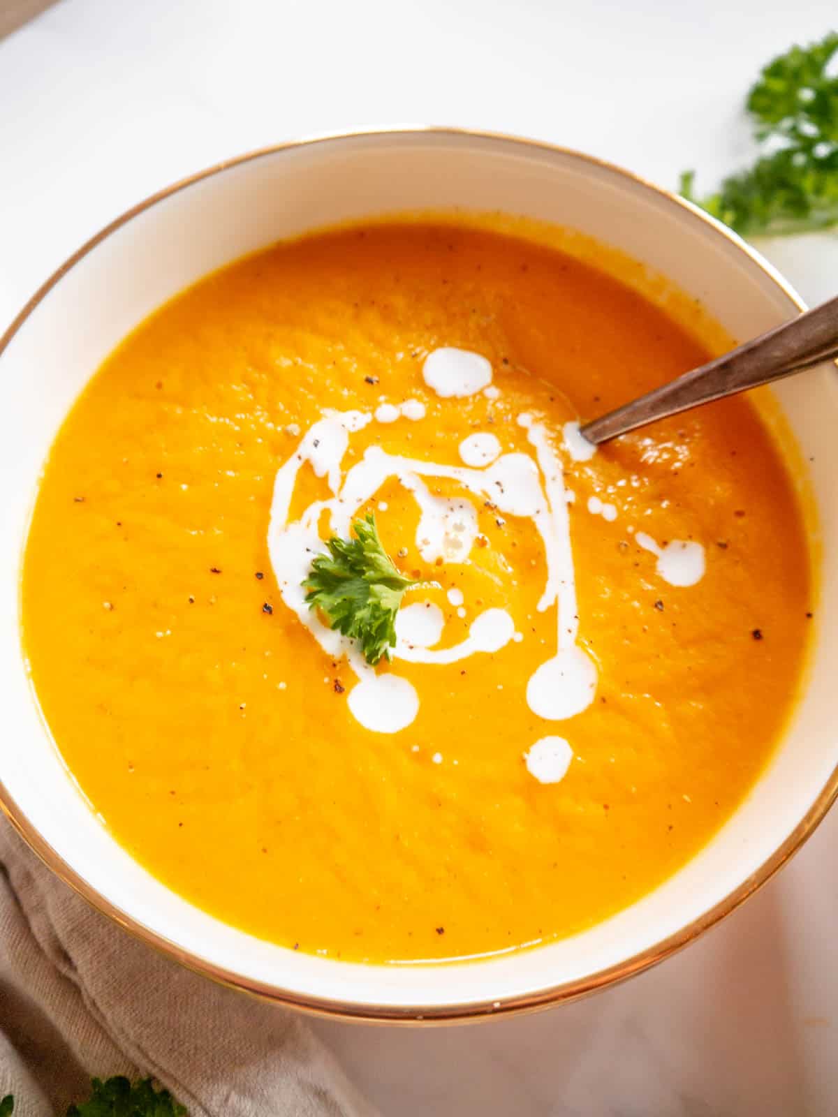 Butternut squash carrot ginger soup in a bowl with cream drizzled on top.