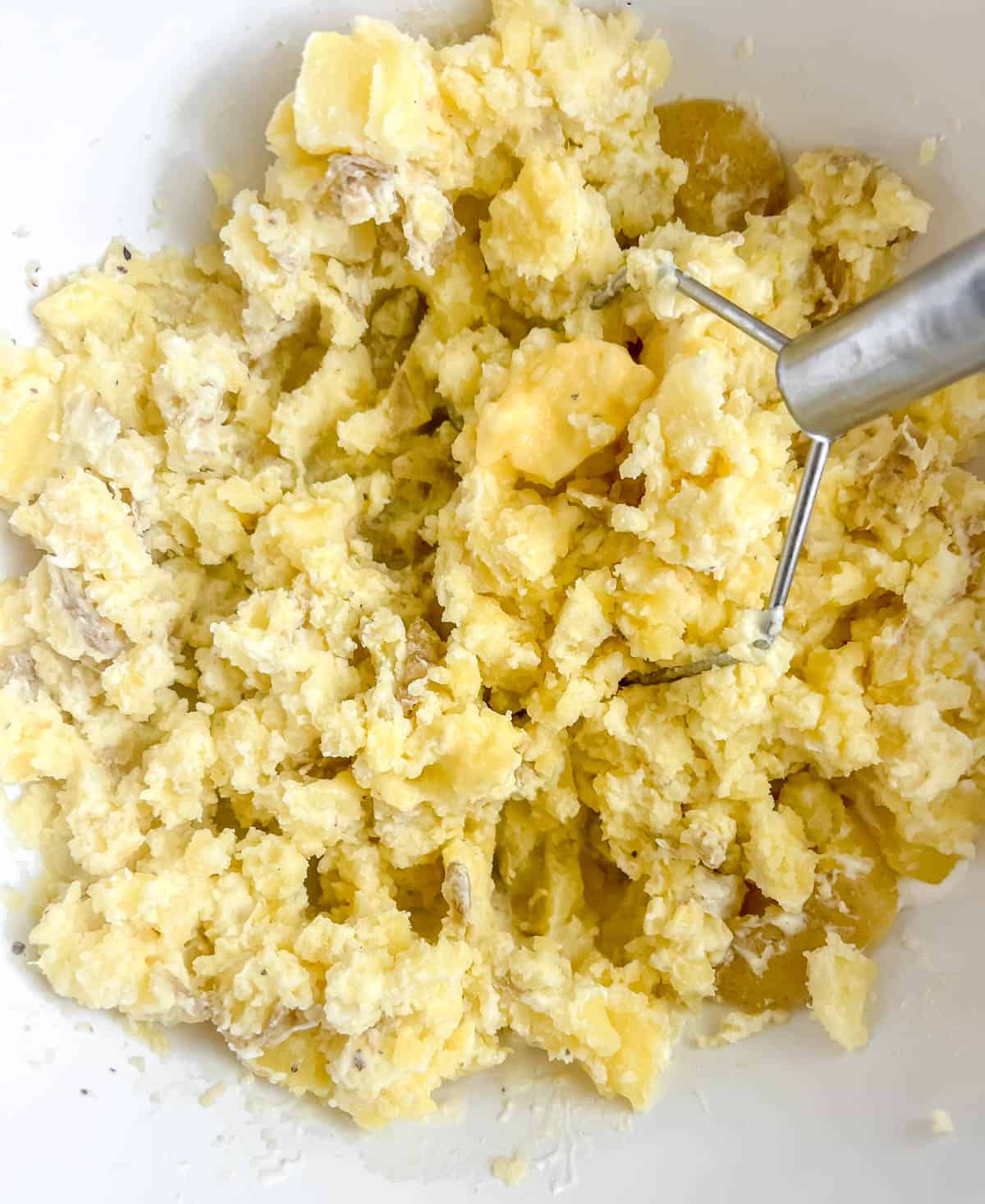 Mashed potatoes with greek yogurt in a bowl with a potato masher.