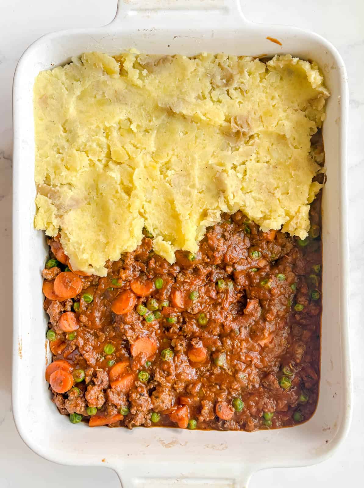 Fluffy mashed potatoes being added to the top of the shepherd's pie filling.
