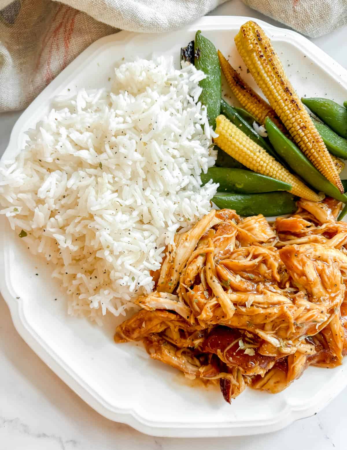 A plate with slow cooker shredded honey garlic chicken with rice and veggies.