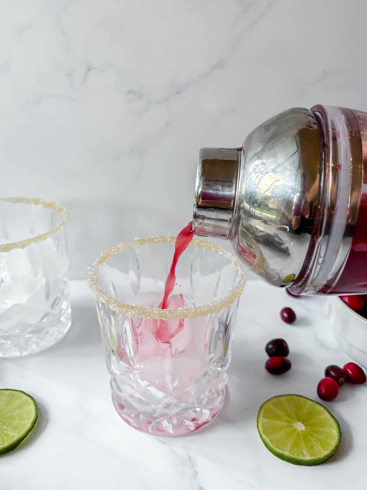 Cranberry margarita being poured into a cup from a cocktail shaker.